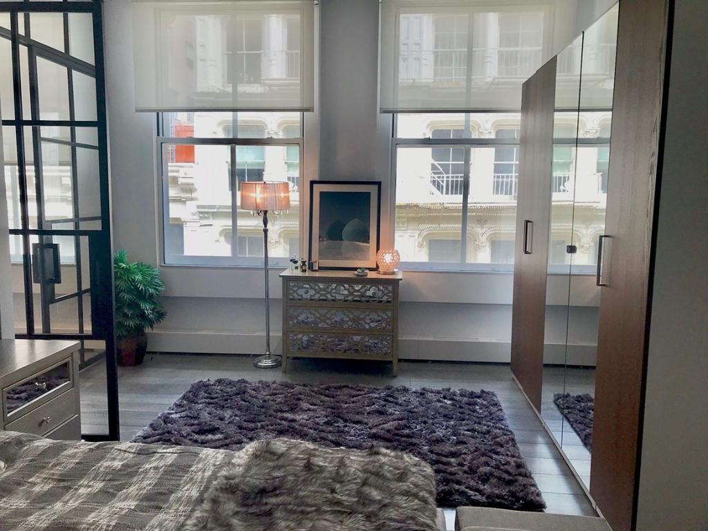Styled bedroom with mirrored dresser, shag rug, and city view windows