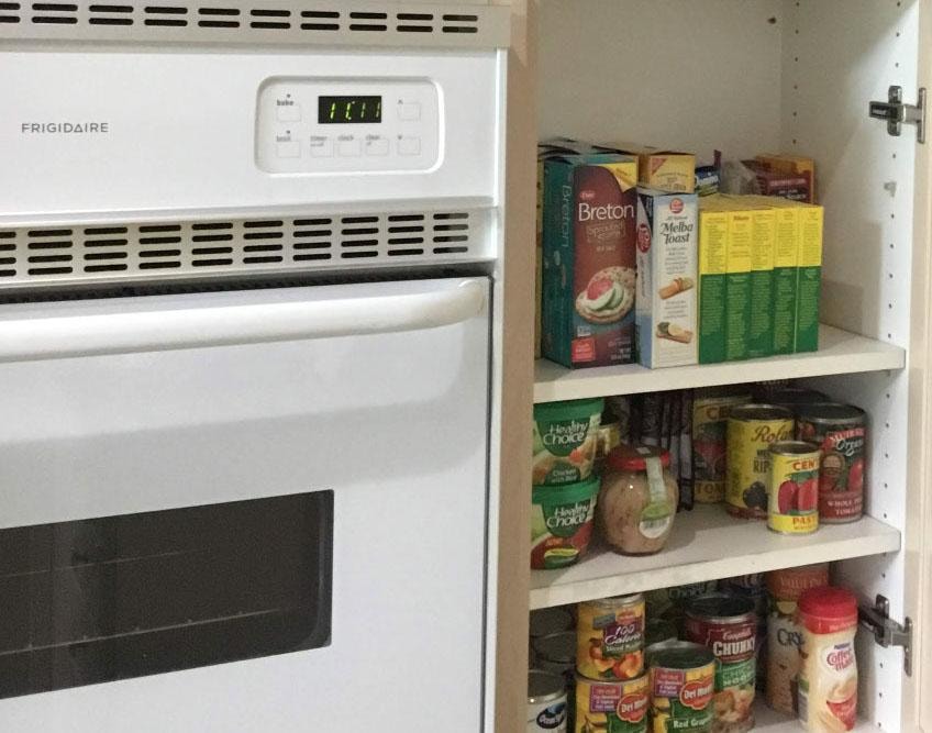 Organized kitchen pantry cabinet with canned goods and dry foods next to oven