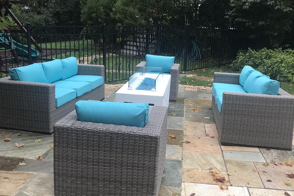 Outdoor patio with gray wicker furniture and turquoise cushions around fire pit